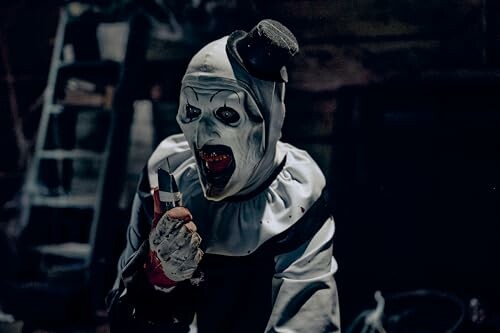 Creepy clown wearing a white outfit and holding a knife in a dark setting.